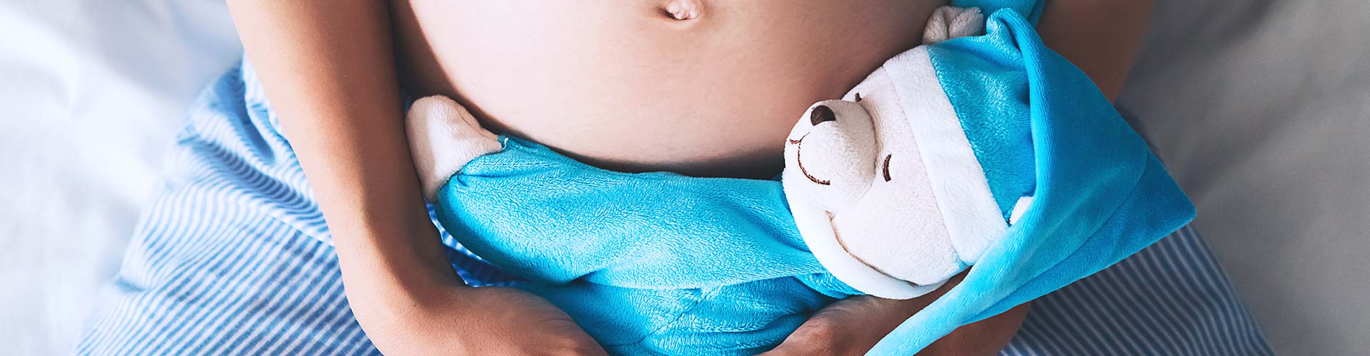 Pregnant woman's belly with teddy toy bear.