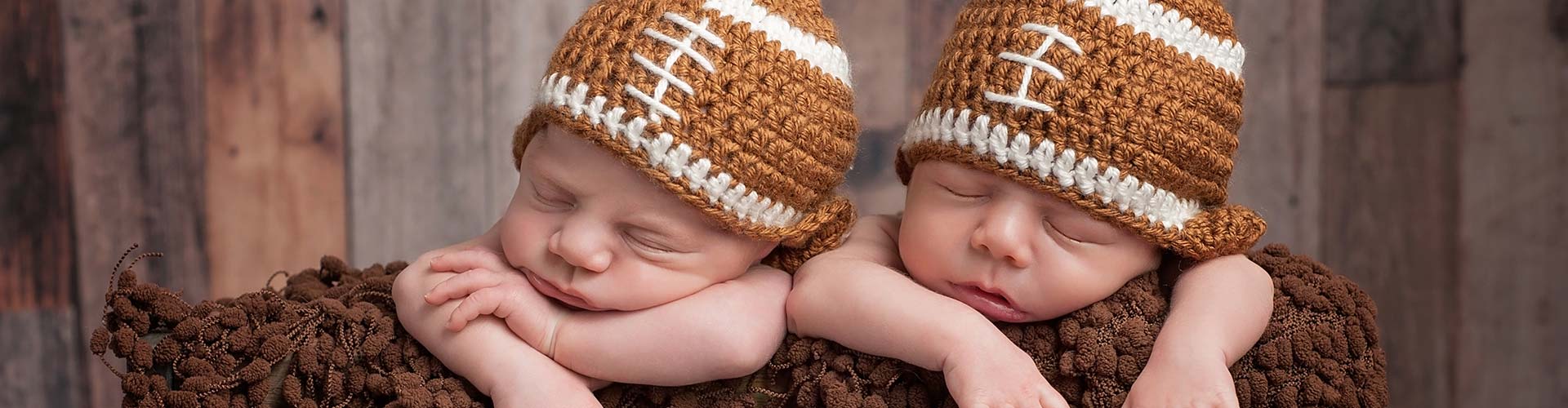 Twin baby boys wearing football shapeds hats.
