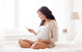 pregnant woman sits on the bed and uses a smartphone